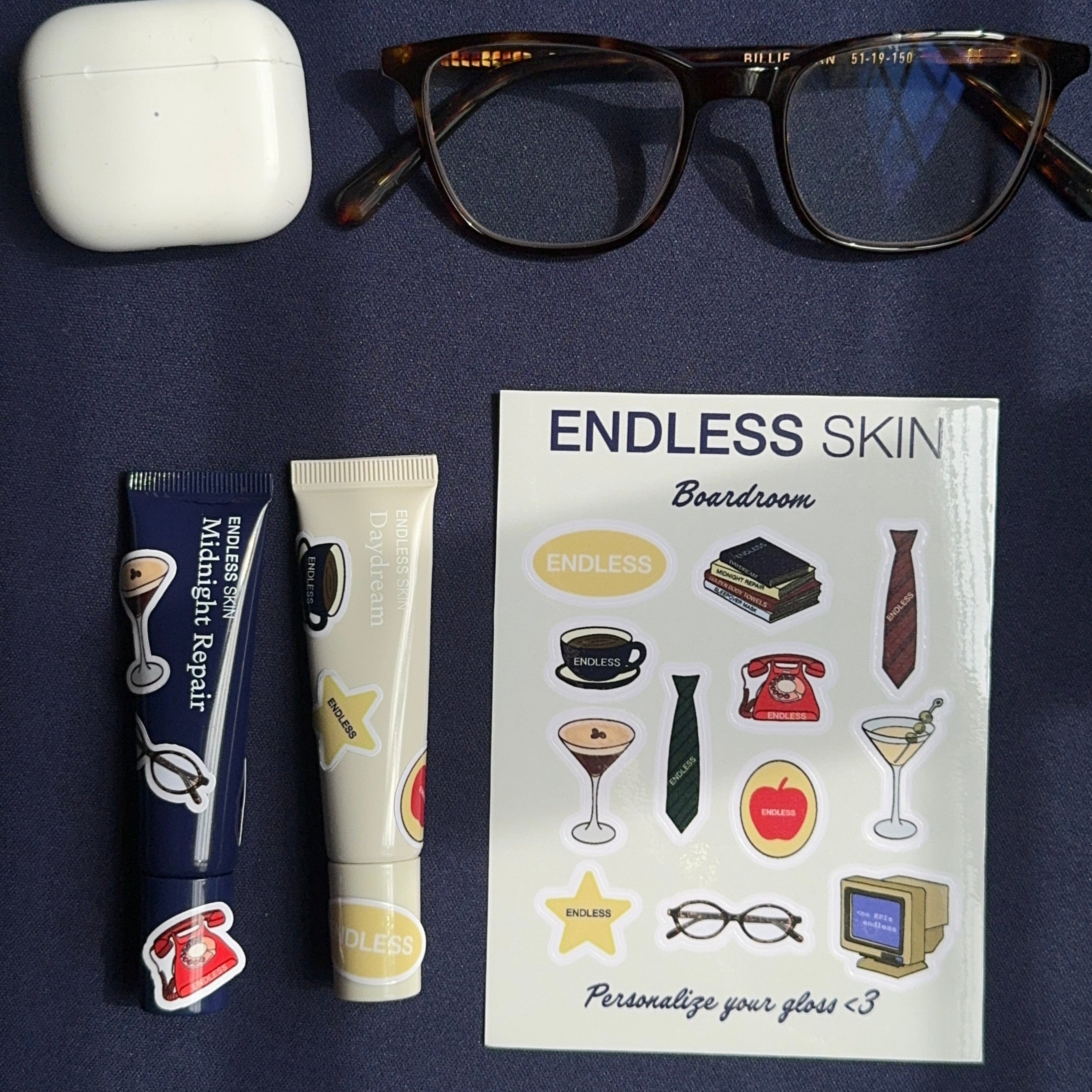 Sheet of tattoos labeled 'Endless Skin' with a pair of glasses, airpods, and a tube of lip balm on a dark surface.